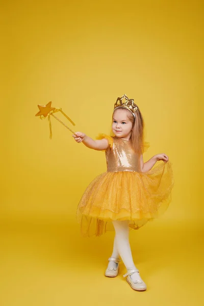 一个快乐的小女孩 留着一头长长的头发 金黄色的裙子 头戴王冠 背景是黄色的魔杖 为孩子们庆祝一个五彩缤纷的嘉年华 表达积极的生日 — 图库照片