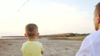 Oğlan ve baba uçurtma uçuruyorlar kumsalda yavaş çekimde zaman geçiriyorlar.
