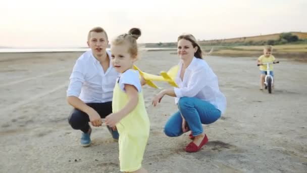 Mädchen spielt mit Flugzeug, während Familie auf Seeküste Zeitlupe — Stockvideo