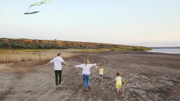 Joven familia corre volando cometa a lo largo de arena costa cámara lenta — Vídeo de stock