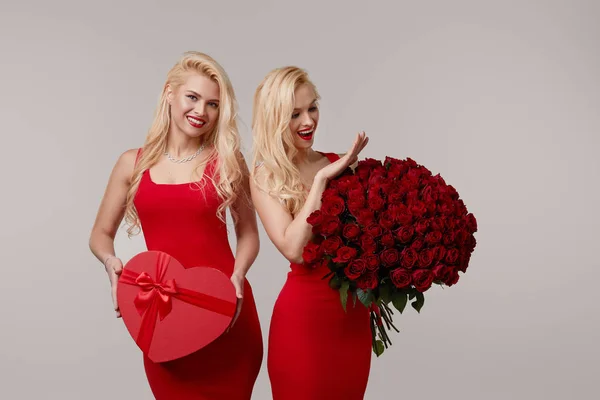 Δύο Χαρούμενες Νεαρές Δίδυμες Γυναίκες Ένα Μεγάλο Μπουκέτο Κόκκινα Τριαντάφυλλα — Φωτογραφία Αρχείου