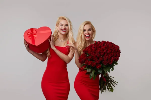 Δύο Χαρούμενες Νεαρές Δίδυμες Γυναίκες Ένα Μεγάλο Μπουκέτο Κόκκινα Τριαντάφυλλα — Φωτογραφία Αρχείου