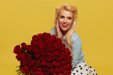 Eski moda elbiseli genç bir kadın parlak sarı bir arka planda büyük bir buket kırmızı gül tutuyor. Sevgililer Günü ve 8 Mart için hediye konsepti..