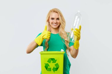 Yeşil tişört ve eldiven giyen genç bir kadın geri dönüşüm için plastik atık topluyor. Beyaz stüdyo geçmişi