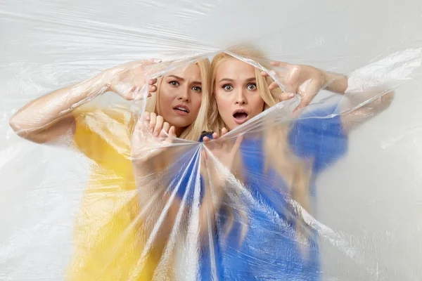 年轻的女性志愿者穿着黄色和蓝色的T恤衫站在一面由不可降解的聚乙烯包裹的墙壁上 试图与玻璃纤维作斗争 废物循环再用概念 — 图库照片