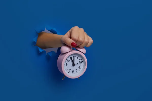 Wake up. Pink alarm clock in hand through a torn dark blue paper wall, mockup. Space for text. Run out of time. Fail deadline. The concept of time management and discipline