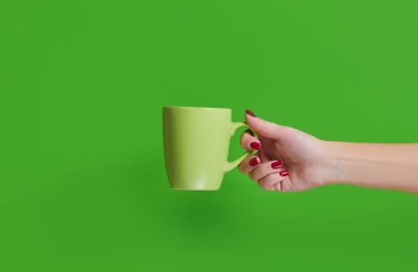 Kadının elinde yeşil bir seramik bardak ve yeşil bir arka plan var.