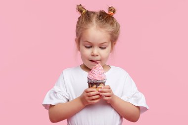 Zevkli şirin bir kız çocuğu pembe stüdyo arka planında lezzetli dondurmalar yiyor. Kapalı gözlerle yalamak. Bebek maması ve mutlu bir çocukluk.
