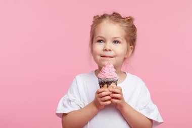 Zevkli şirin bir kız çocuğu pembe stüdyo arka planında lezzetli dondurmalar yiyor. Kapalı gözlerle yalamak. Bebek maması ve mutlu bir çocukluk.