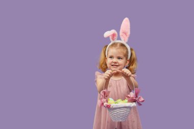 Kostümlü Paskalya tavşanı kulaklı ve yumurtalı sepetli mutlu kız çocuğu. Mor arka planda küçük bir kız