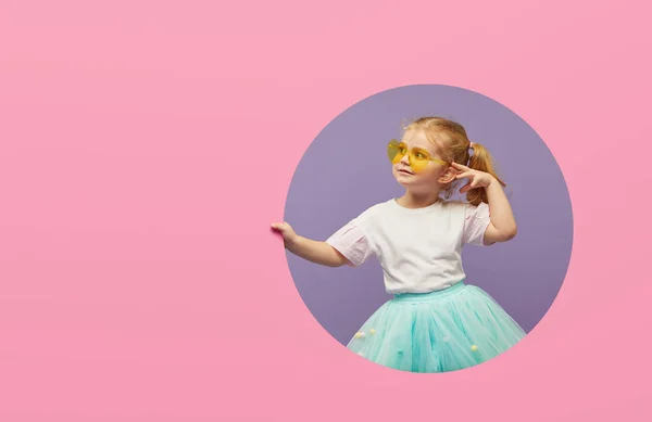 令人惊讶的小女孩戴着心形的太阳镜 从粉红色的圆孔里往外看 快乐的女孩看着相机 哇可笑的脸 — 图库照片