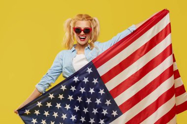 American girl. Happy young woman in denim clothes holding USA flag isolated on yellow background