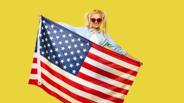 American girl. Happy young woman in denim clothes holding USA flag isolated on yellow background
