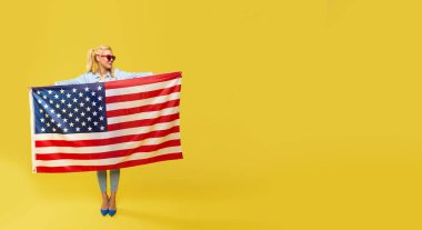 Amerikalı kız. Sarı arka planda Usa bayrağı taşıyan kot elbiseli mutlu genç kadın. Pankart. Metin için alanı kopyala