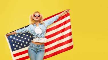 American girl. Happy young woman in denim clothes holding USA flag isolated on yellow background