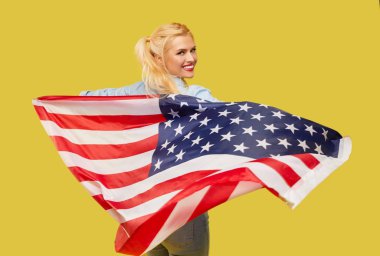American girl. Happy young woman in denim clothes holding USA flag isolated on yellow background
