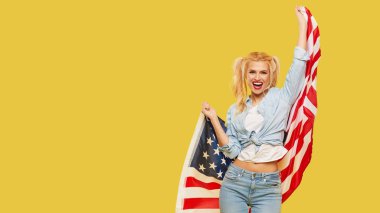 American girl. Happy young woman in denim clothes holding USA flag on yellow background. Banner. Copy space for text. football fan