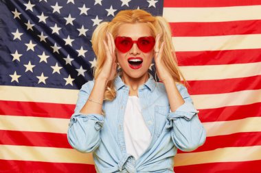 American girl. Happy young woman in heart shape sunglasses on USA flag  background. Funny and surprised human face. Patriotism concept