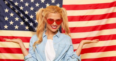 American girl. Happy young woman in heart shape sunglasses on USA flag  background. Funny and surprised human face. Patriotism concept