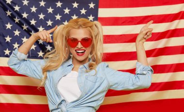 American girl. Happy young woman in heart shape sunglasses on USA flag  background. Funny and surprised human face. Patriotism concept