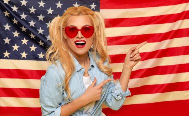 American girl. Happy young woman in heart shape sunglasses on USA flag  background. Funny and surprised human face. Patriotism concept