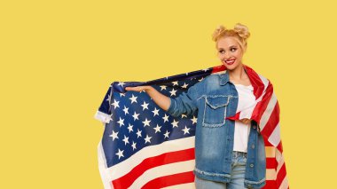 American girl. Happy young woman in denim clothes holding USA flag isolated on yellow background. Banner. Empty space for text