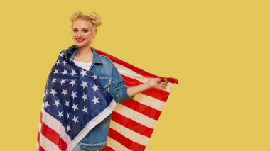 American girl. Happy young woman in denim clothes holding USA flag isolated on yellow background. Banner. Empty space for text