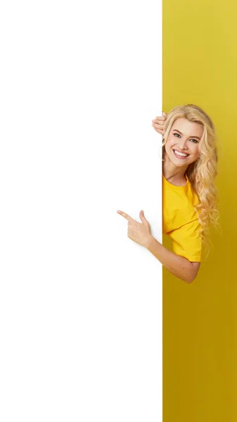 Young Happy Woman Peeks Out White Banner Yellow Background Point — 스톡 사진