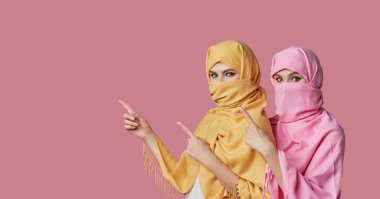 Kız gücü. Pembe arka planda renkli tesettürlü iki Müslüman kadın. Parmakla işaret ediyor. Metin için boşluk