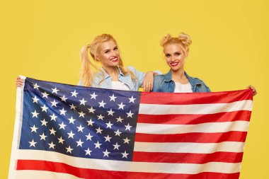 Amerikalı kızlar. Sarı arka planda Usa bayrağı taşıyan kot elbiseli mutlu genç kadınlar. futbol hayranı