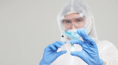 Biological hazard. Epidemic of the Chinese coronavirus. An asian woman in a protective suit and mask holds an injection syringe and vaccine. Vaccine from, flu, coronavirus, ebola, TB. 