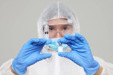Biological hazard. Epidemic of the Chinese coronavirus. An asian woman in a protective suit and mask holds an injection syringe and vaccine. Vaccine from, flu, coronavirus, ebola, TB. 