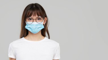Asian woman feeling unwell and wearing face protective mask on grey studio background. Copy space for text. The first defense against the epidemic of flu and coronavirus