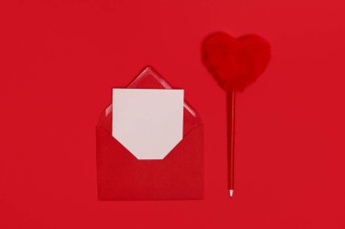 Valentines Day. Blank template for romantic letters in an envelope on a red background. Fluffy red heart shaped pen. Flat lei. View from above.