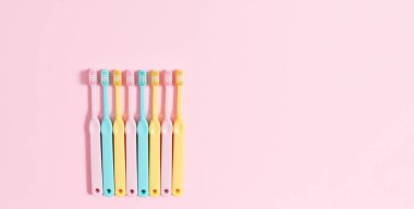 Dişlerini fırçalama zamanı. Ağız temizliği. Pembe arka planda çalar saati olan bir sürü renkli diş fırçası. Üst manzara, düz uzanma