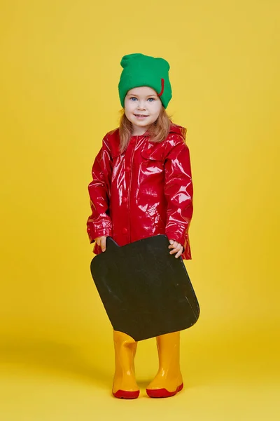 黄色の背景に黒い黒板のバナーを持っている小さな子供の女の子 面白い顔だ テキストのスペースをコピーします 季節の子供製品の広告 — ストック写真
