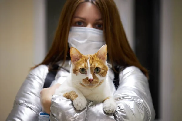 Koruyucu maskeli genç bir kadın kollarında maskeli bir kedi tutuyor. Koronavirüs salgınına karşı savaşan bilinçli vatandaş.