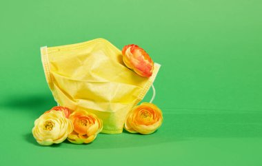 Yeşil arka planda taze çiçekli sarı koruyucu tıbbi maske. Virüs ve karantina mevsimi eğilimi