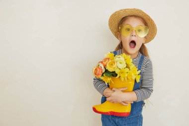 Lastik botunda sarı çiçekleri olan hasır şapkalı küçük bir kız çocuğu. Annemin küçük yardımcısı bahçedeydi. Metin için alanı kopyala