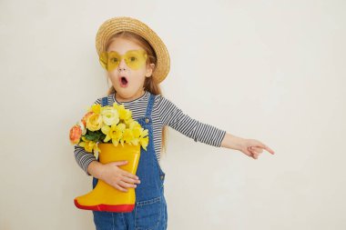 Lastik botunda sarı çiçekleri olan hasır şapkalı küçük bir kız çocuğu. Annemin küçük yardımcısı bahçedeydi. Metin için alanı kopyala