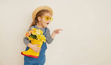 Lastik botunda sarı çiçekleri olan hasır şapkalı küçük bir kız çocuğu. Annemin küçük yardımcısı bahçedeydi. Metin için alanı kopyala