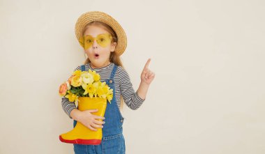 Lastik botunda sarı çiçekleri olan hasır şapkalı küçük bir kız çocuğu. Annemin küçük yardımcısı bahçedeydi. Metin için alanı kopyala