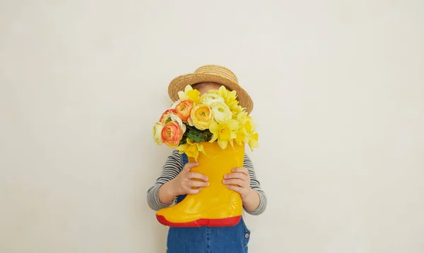 ゴム製のブーツに黄色の花の花束とわらの帽子の小さな驚きの子供の女の子 ママは庭ではほとんど助けにならない テキストのコピースペース — ストック写真
