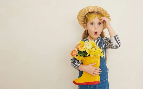 ゴム製のブーツに黄色の花の花束とわらの帽子の小さな驚きの子供の女の子 ママは庭ではほとんど助けにならない テキストのコピースペース — ストック写真