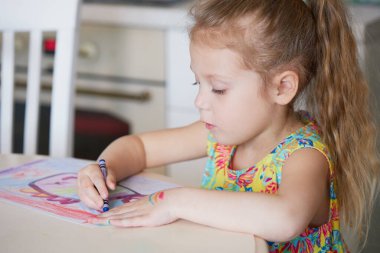 Çocukların yaratıcılığı. Küçük kız evde balmumu kalemlerle resim çiziyor. Küresel karantina dönemi için çevrimiçi uzaklık öğrenme kavramı.