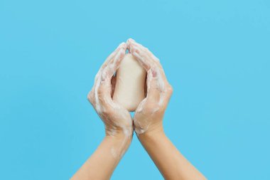 Hand hygiene concept. Female hands are holding antibacterial soap with foam on a blue background. Hand antiseptic during the coronovirus pandemic clipart