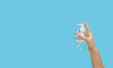 Sıvı alkol antiseptik jel kullanan kadın elleri, koronavirüs salgınını önler, mavi arka planda el dezenfektanı ile ellerini yıkayan kadın.