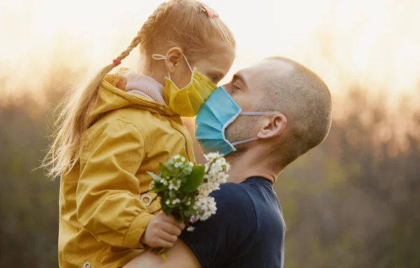 家庭保护 一位年轻的父亲在室外的春天花园拥抱他的小女儿 面部防护口罩 防止感染头孢病毒 — 图库照片