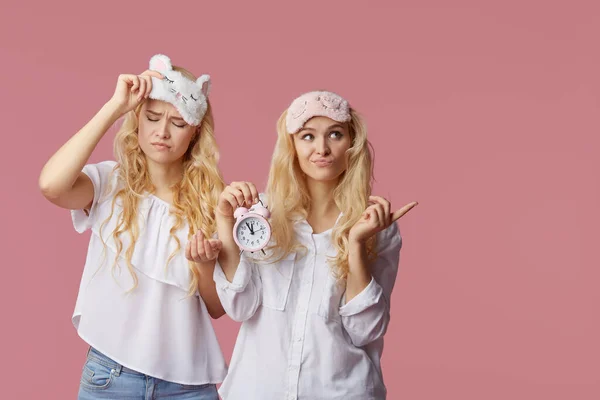 Två Sömnlösa Unga Kvinnor Pyjamas Och Sömnmasker Rosa Bakgrund Väckarklockan — Stockfoto