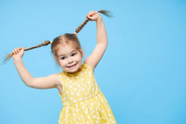 Şaşırmış, gülümseyen küçük bir kızın portresi. Çocuk mavi arka planda tek başına duruyor. Kameraya bakıp gülüyorlar.